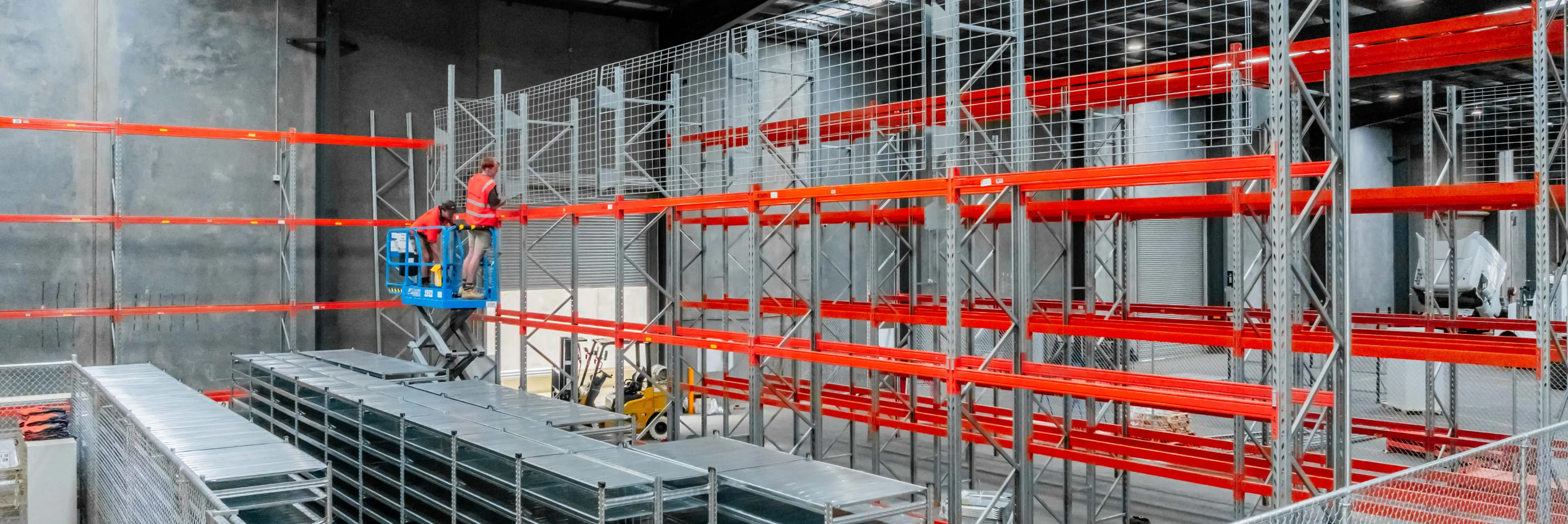 Warehouse racking installation with scissor lift and technicians assembling storage system